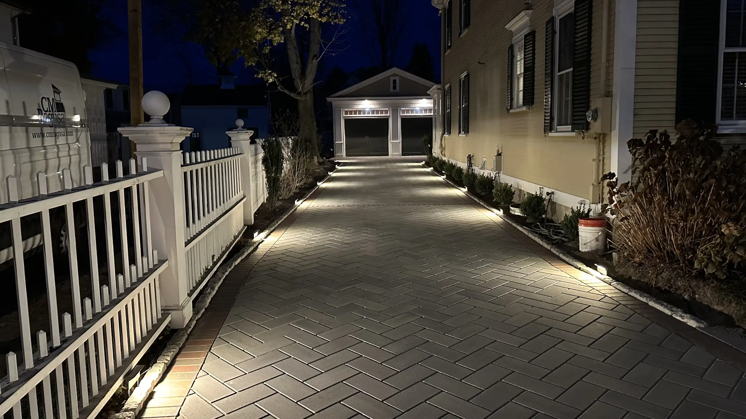Low voltage landscape lighting illuminating a custom paver driveway built by Outdoor Lifestyles